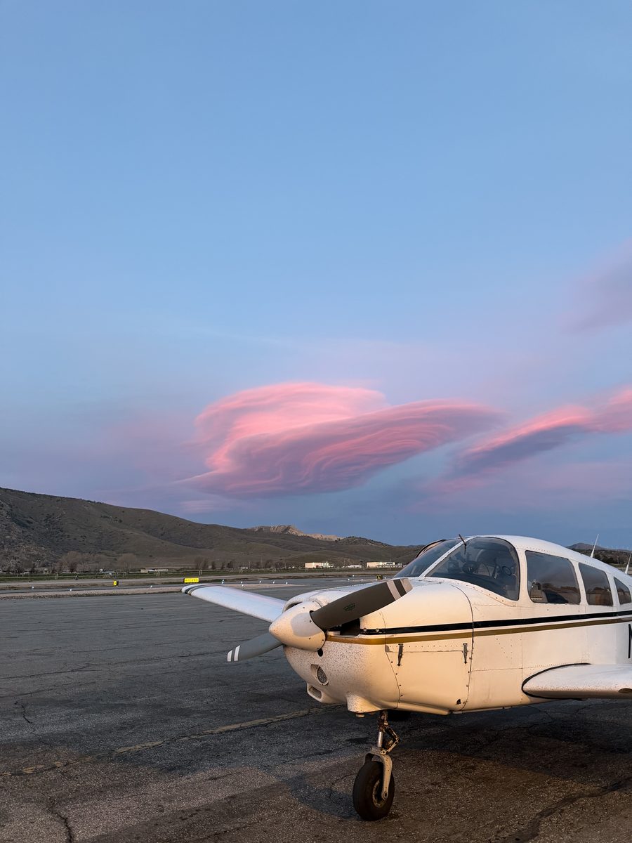 A Piper Warrior on the ramp beneath a pink lenticular cloud at sunset